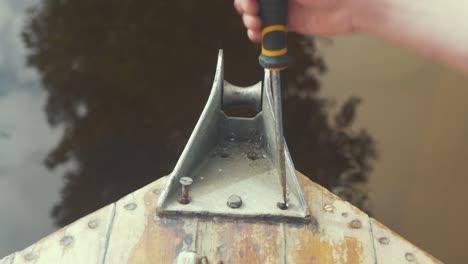 Close up view, man removing bow roller with screwdriver from old wooden boat