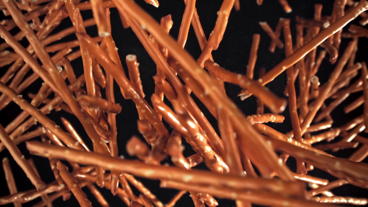 Bastoncini di pretzel che cadono in super slow motion su sfondo nero.