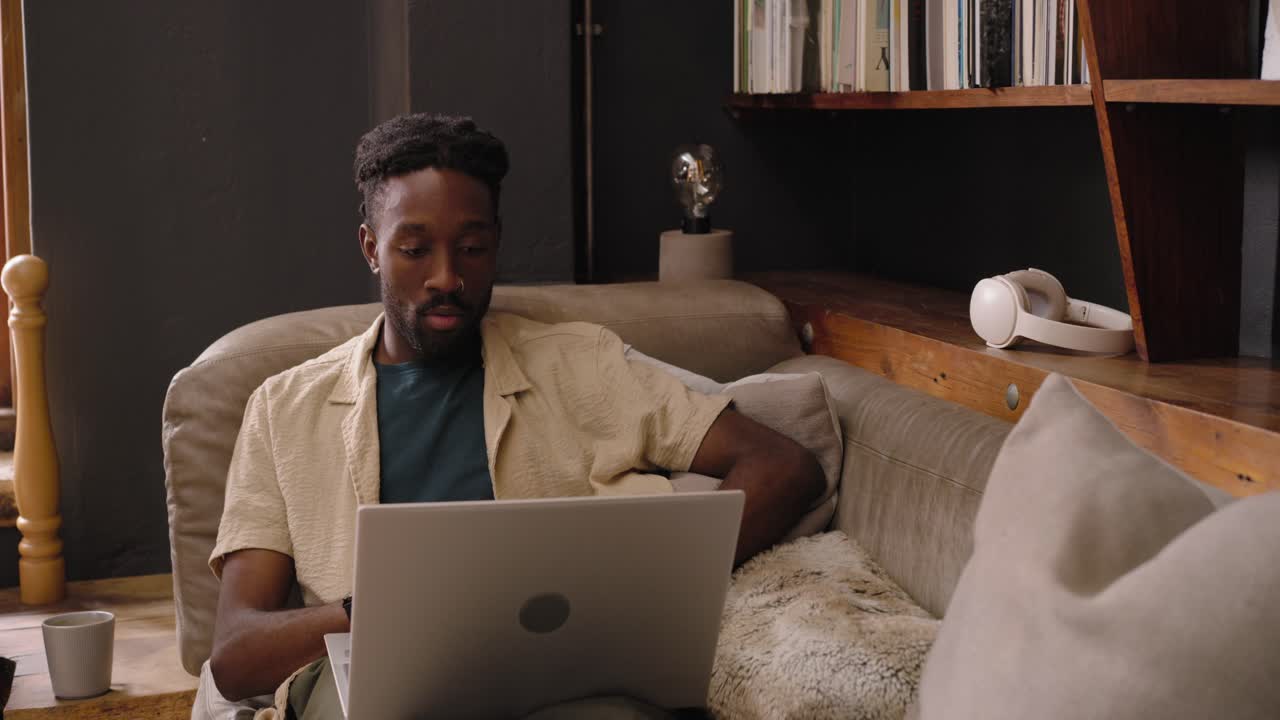 Adult African man reclining on sofa at home finishing laptop work closing laptop stretching resting