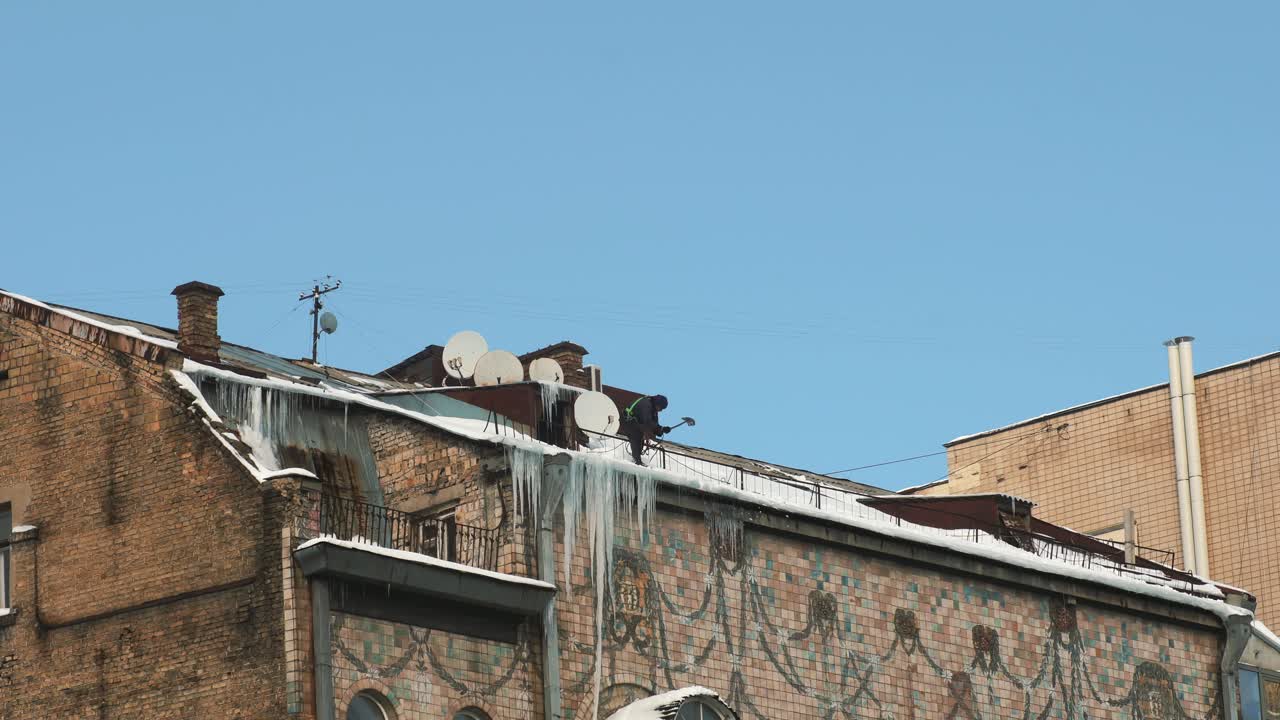 Lavoratore che pulisce neve e ghiaccio dal tetto di un edificio
