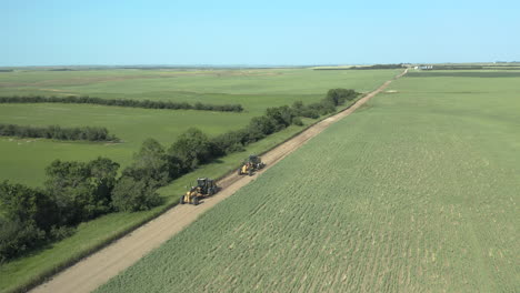 Road-graders-leveling-long-straight-dirt-road,-Saskatchewan,-Canada