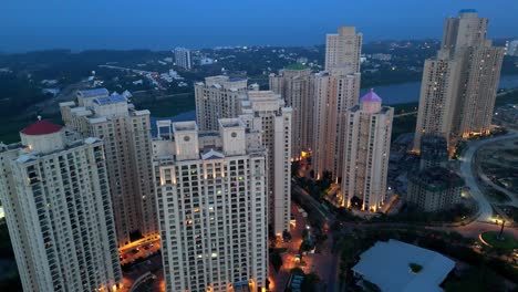 high-angle aerial view of a modern residential township at dusk hiranandani parks india. the scene is dominated by numerous high-rise apartment towers with illuminated windows