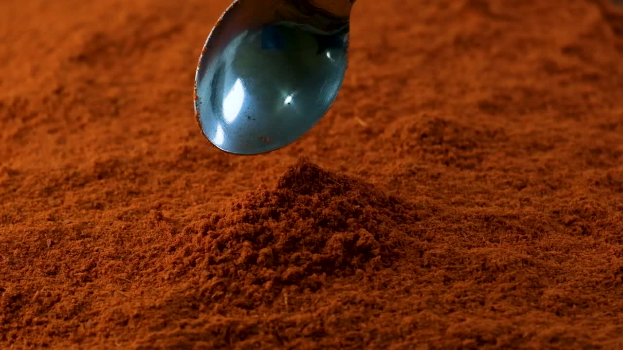 Silver spoon drops chili powder or paprika onto bigger pile