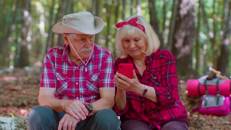 atractivo anciano hombre mujer mochilero planeando una ruta de viaje en el bosque en el teléfono móvil en el bosque