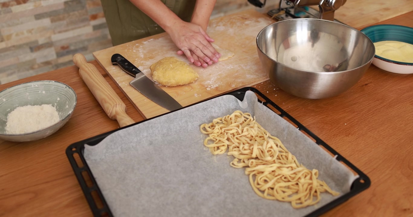 Persona che impasta pasta fresca su un piano cucina in legno