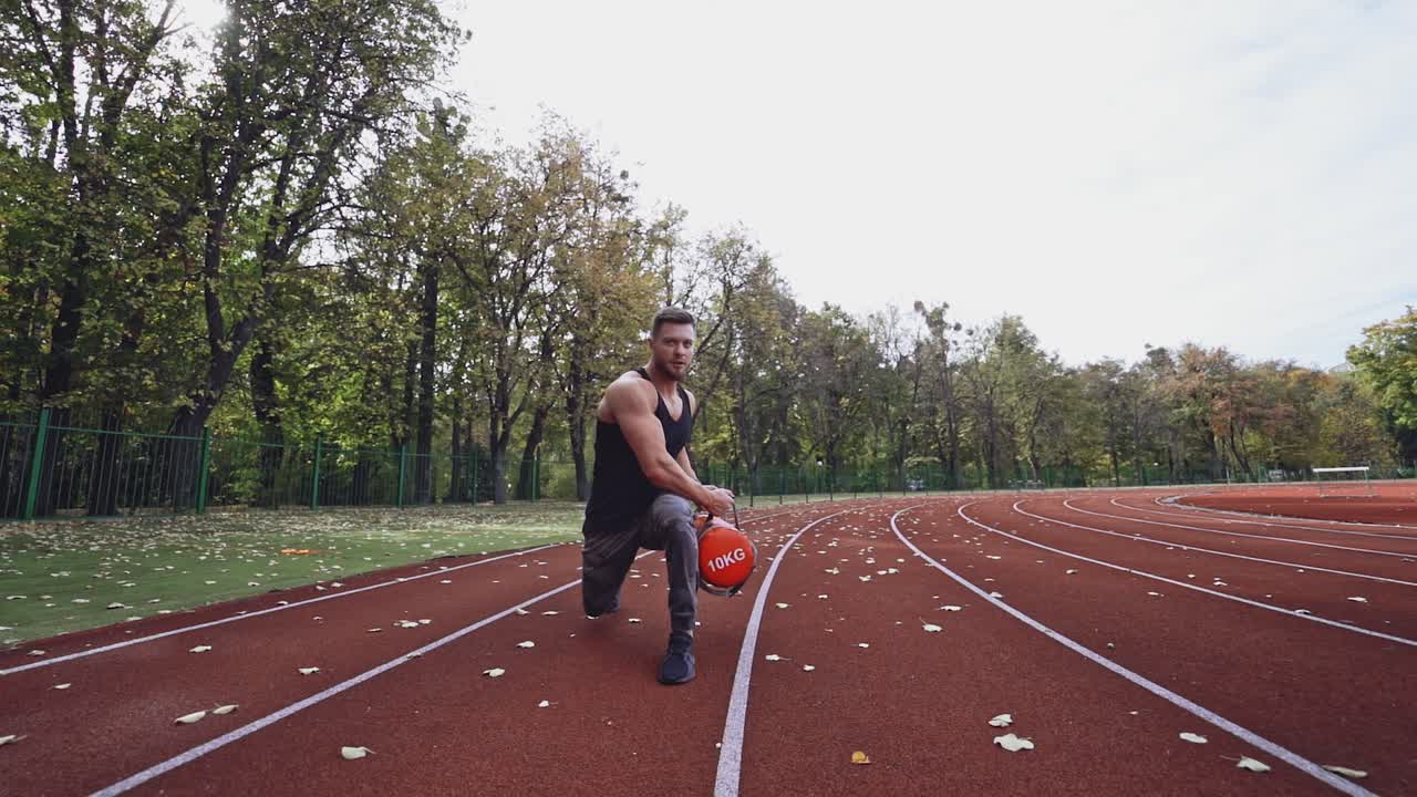 Athlete is doing workout in open air. Muscular sportsman lifting weights on the stadium in autumn daytime. Slow motion.