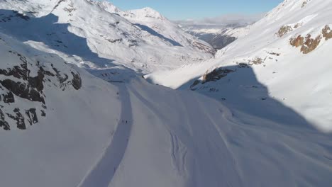 Aerial-drone-view-overlooking-downhill-skiers-in-a-stunning-sunny-alpine-landscape