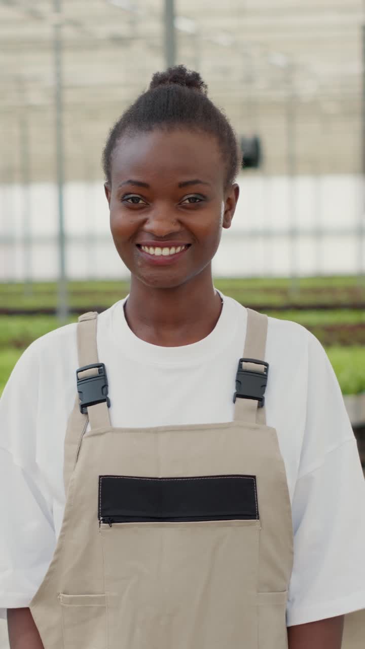 Ritratto di una donna afroamericana che posa felice in una fattoria di colture biologiche e verdure mentre diversi lavoratori spingono casse