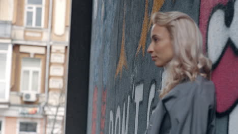 blonde woman looking city view near graffiti wall on urban building.