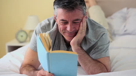 mature man lying on bed reading a book