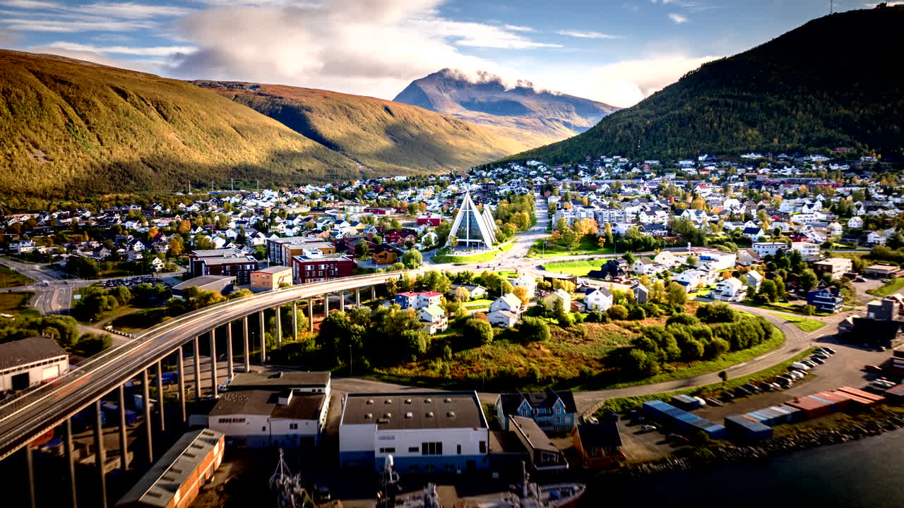 Cinematic drone-hyperlapse, der bevæger sig fremad over Tromsø, Norge, og afslører byens bro, havn og fjordlandskab med dramatisk bjerglys og kyststemning