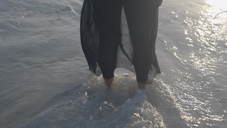 Waves-breaking-on-latina-women-legs-with-black-dress-on-on-the-beach-at-sunset