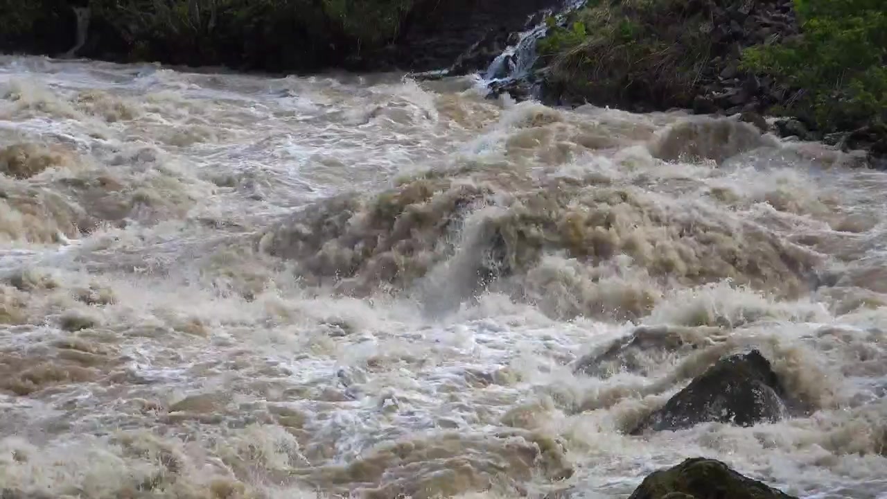 Reißendes, schlammiges Flusswasser fließt über Felsen