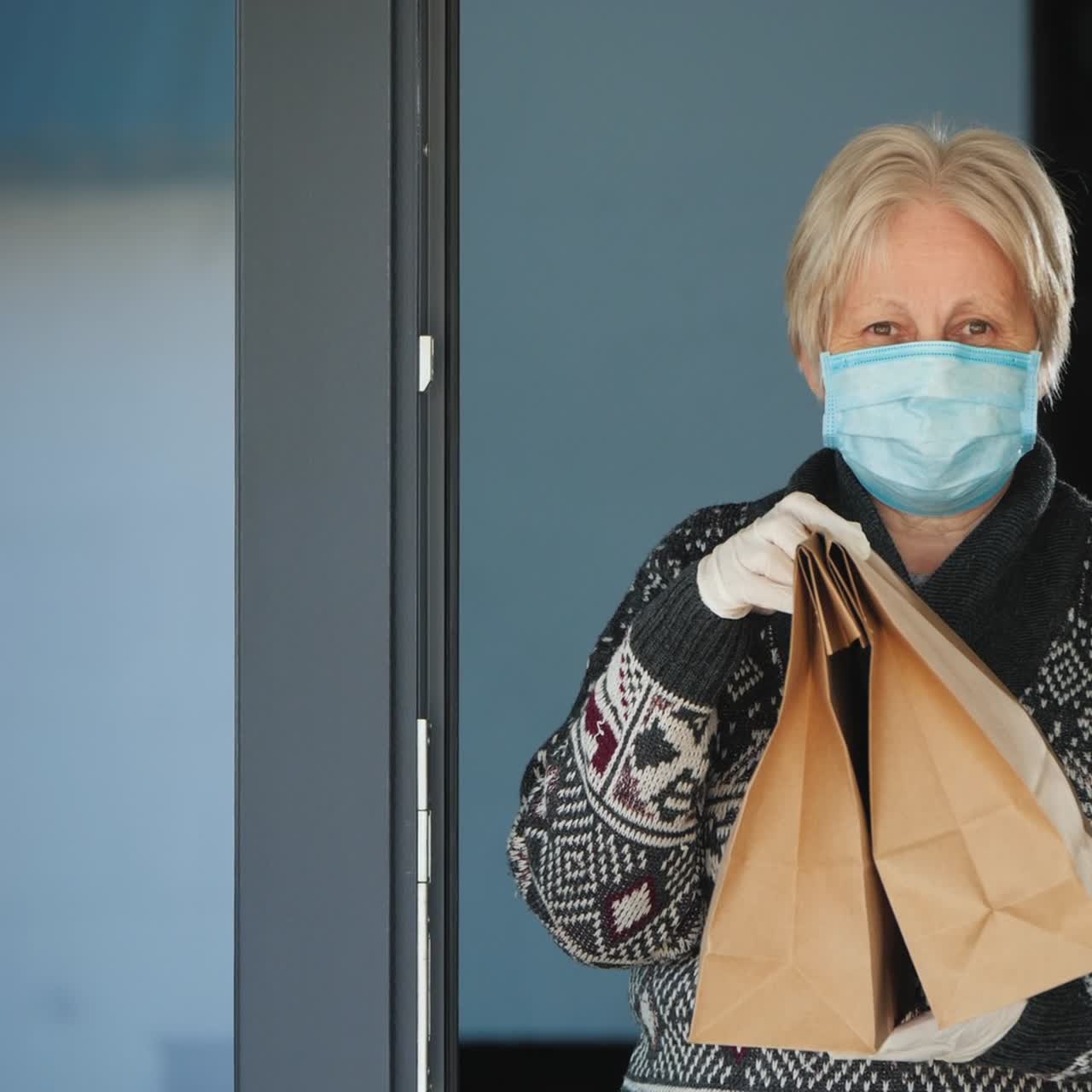 그녀의 집 문앞에 음식 가방을 들고 있는 노인 여성