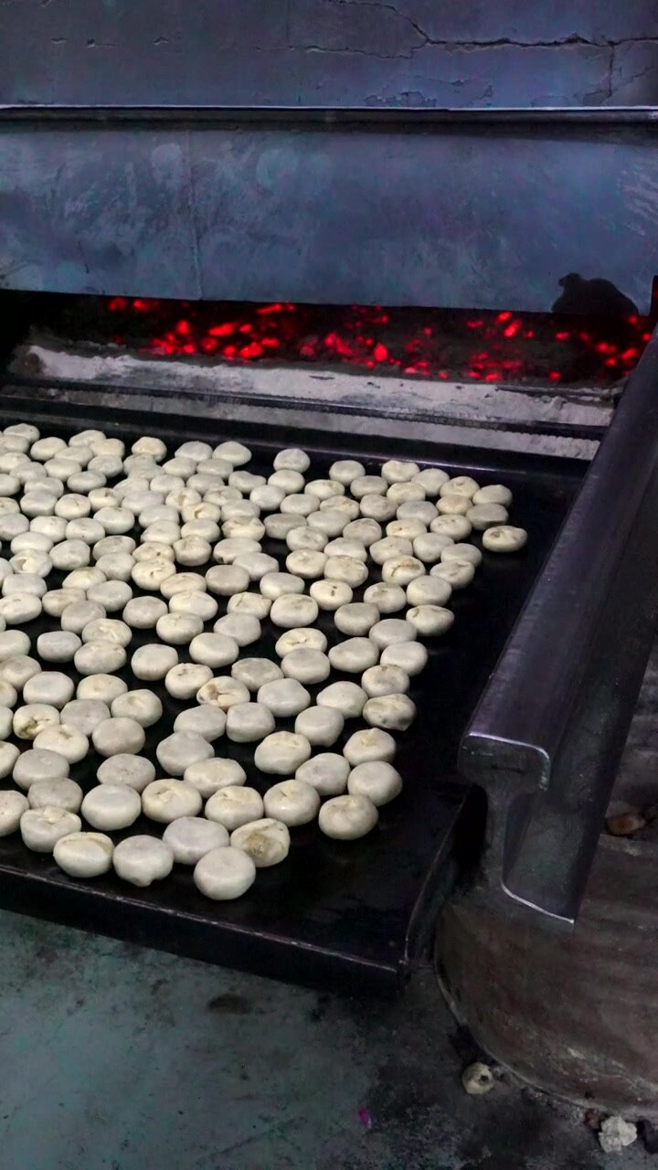 Man inserts batch of Bakpia Pathok pastries into hot oven to bake. Vertical