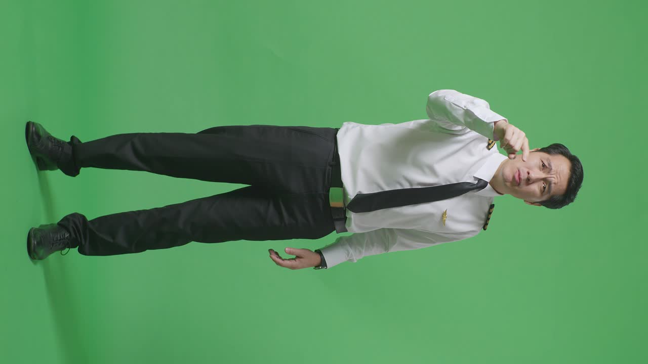 녹색 스크린 배경 스튜디오에 서 있는 동안 카메라에 소리치는 아시아 남성 조종사의 몸이 가득 차 있습니다.