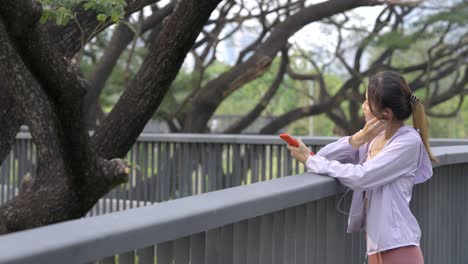 4k young asian woman listening to music from earphones and smartphone while jogging at public park the city in the morning.