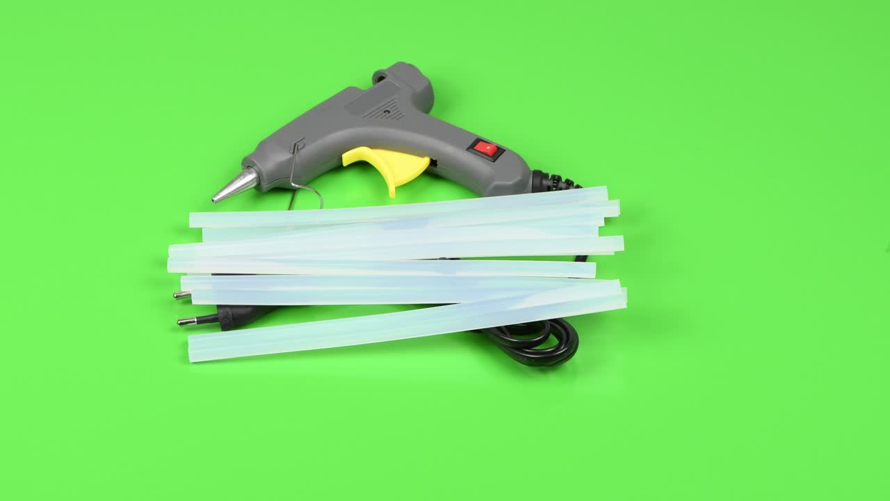 электрический пистолет с горячим клеем и силиконовая палка изолированы на зеленом. боковой вид. петлевое движение. вращение 360.