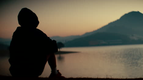 person contemplating sunrise over lake