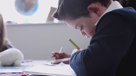 Boy-with-Down-Syndrome-sitting-at-desk-drawing-with-other-kids-in-a-primary-school-lesson,-close-up