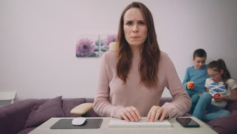 Unhappy-mother-working-on-computer-at-home-with-kids.-Concentrated-woman