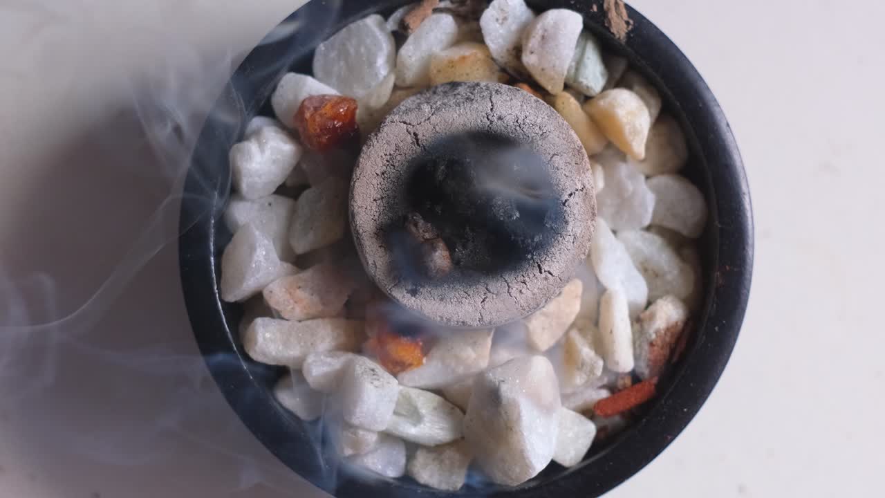 Close up top down view of burning incense with white smoke in a bowl with crystal gemstones, in 4K slow motion