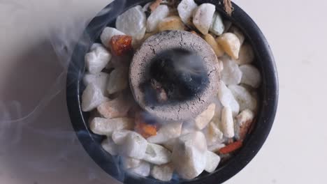 close up top down view of burning incense with white smoke in a bowl with crystal gemstones, in 4k slow motion