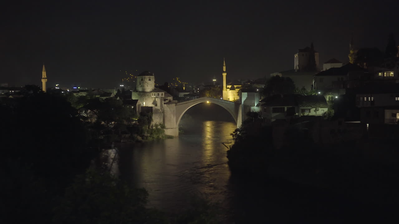 View of Mostar Bridge at Night with city lights on. River seen below.