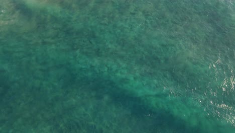 Top-View-Of-Turquoise-Blue-Ocean-Waves-With-Lush-Gorge-Reveal