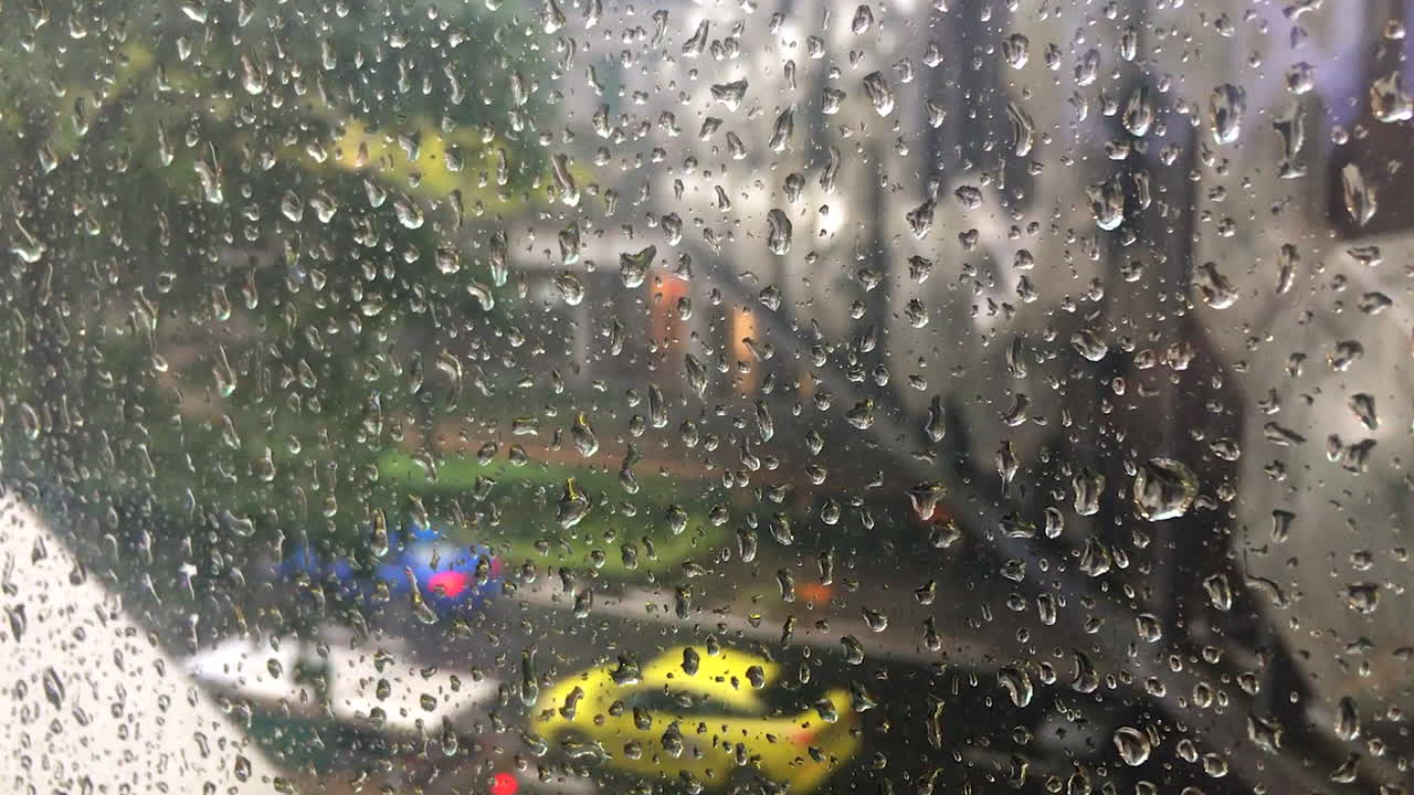Rain drops on glass window panel in city while cars move in background