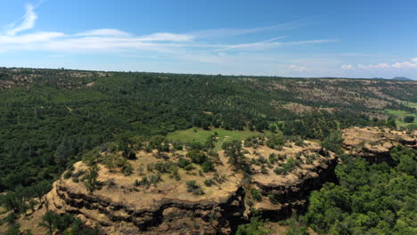 Aerial-rotating-turn-over-red-rock-bluffs-exposing-lush-green-alfalfa-and-hay-fields-in-rural-Tehama-County,-Northern-California