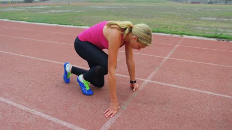 side view of young caucasian female athlete taking starting position on running track 4k