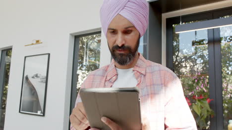 using tablet, man in turban standing indoors, focusing on screen