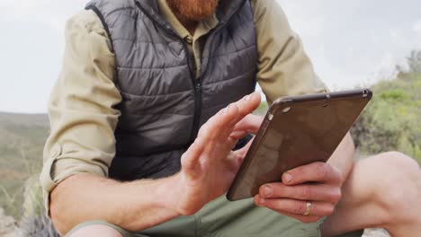 mid section of caucasian male survivalist sitting on mountain, using tablet