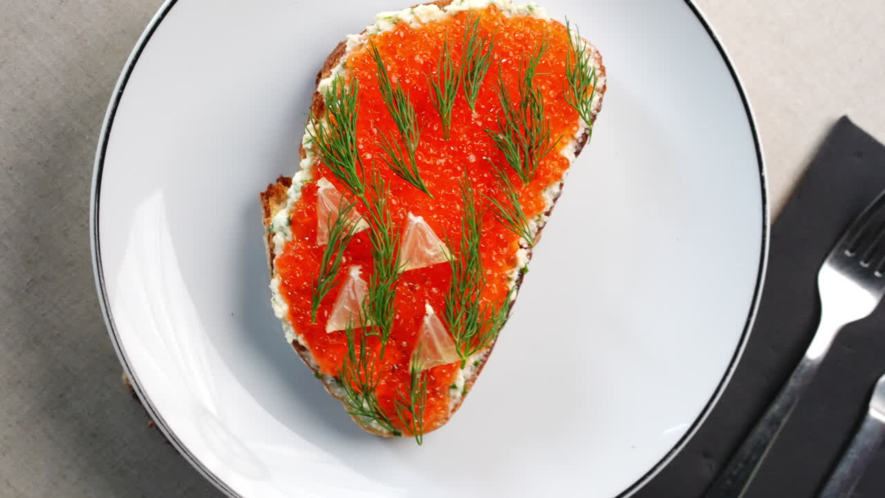 Luxurious appetizer featuring crispy toast layered with creamy cheese, vibrant red caviar, delicate dill sprigs, and zesty grapefruit slices on pristine white plates