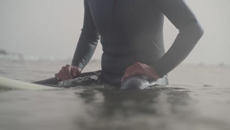 Unrecognizable-surfer-in-wetsuit-sits-on-surfboard-waiting-for-waves,-Sea-level-shot,-Slow-motion