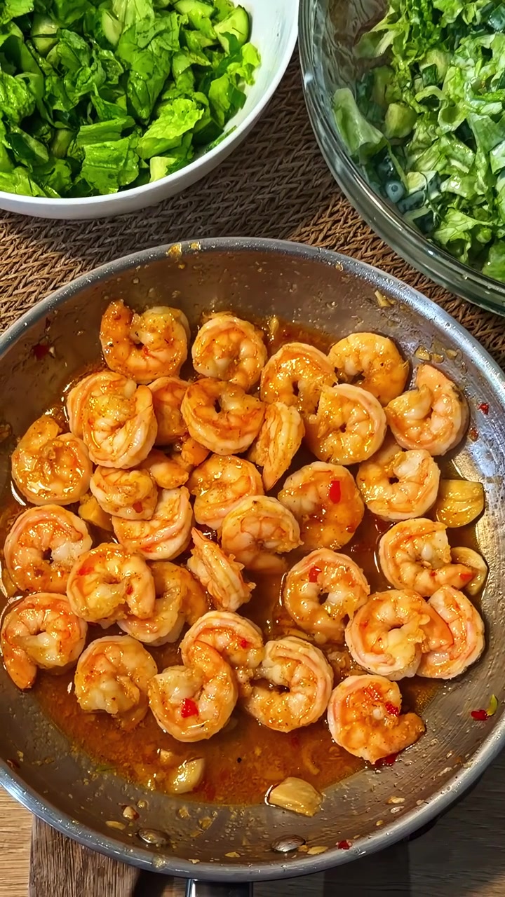 Piatto di gamberi scottati e conditi e ciotola di insalata verde a foglia. - inquadratura dall'alto, verticale.