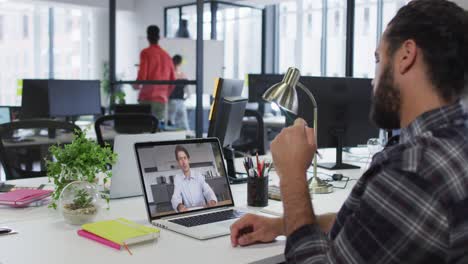 hombre de negocios de raza mixta sentado en un escritorio usando una computadora portátil haciendo una videollamada con un colega masculino