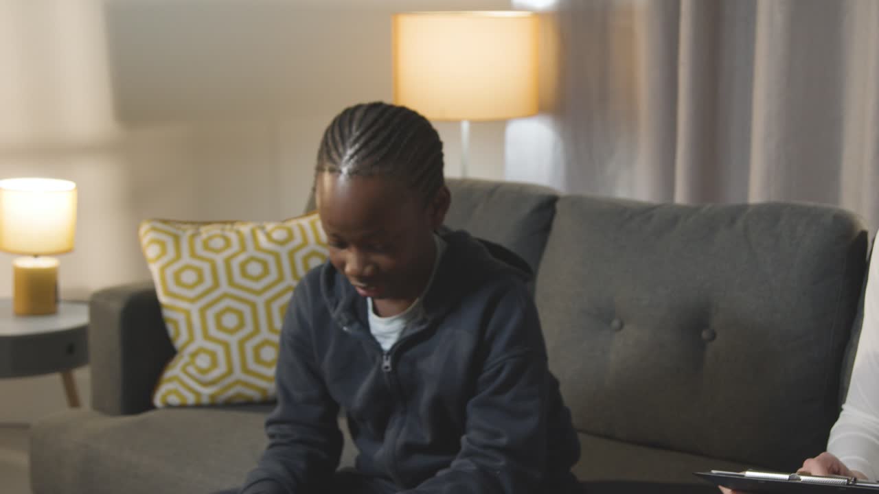 Boy On ASD Spectrum Being Helped Or Assessed By Female Teacher Or Educational Psychologist At Home 4