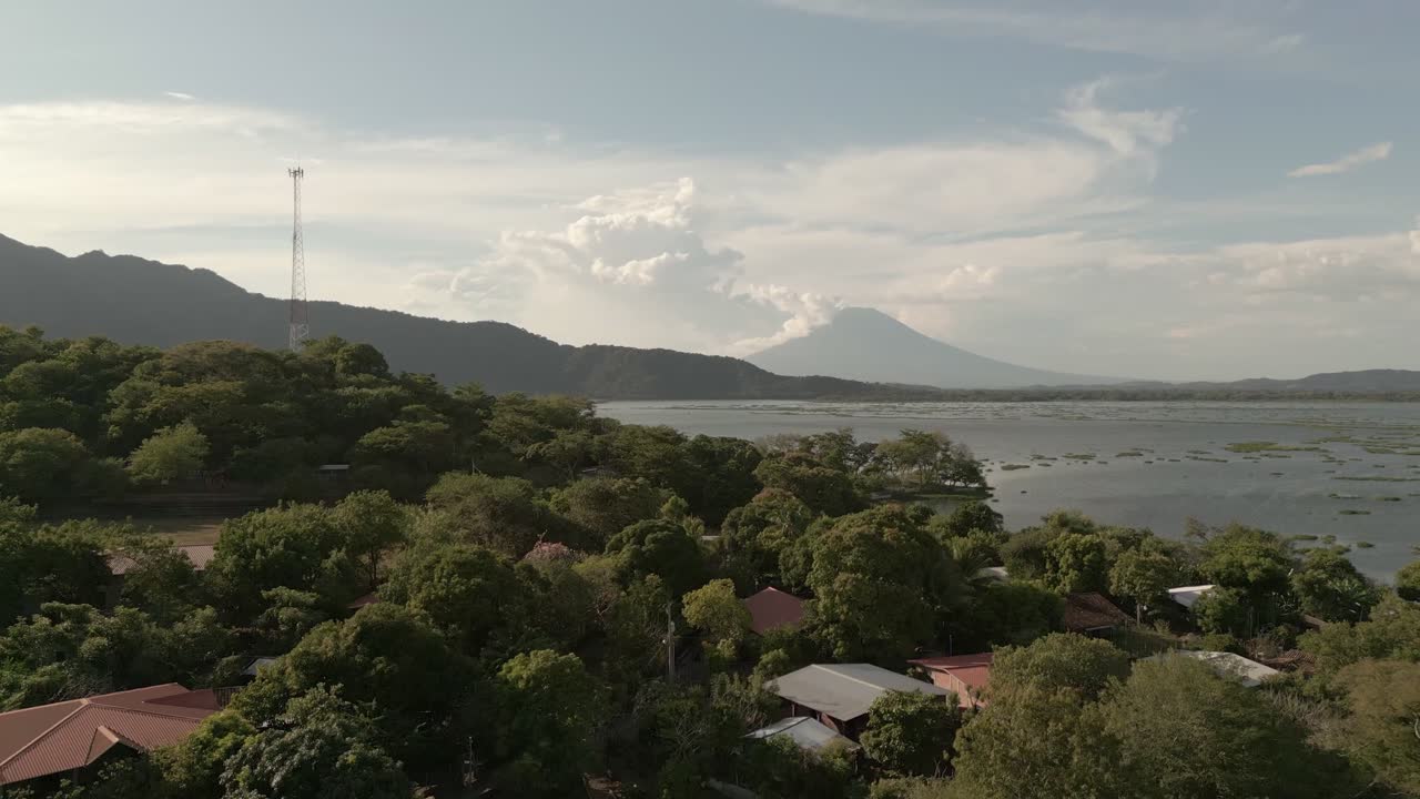 Lush green landscape with scattered houses, a lake, and a distant volcano in view