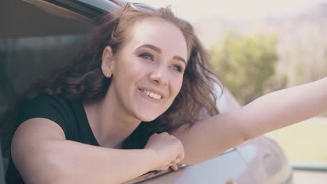 smiling lady looks out of car window waves hands on warm day