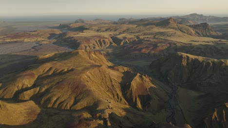 an expansive aerial view of thakgil, iceland, highlighting vast volcanic ridges, winding valleys, and dynamic textures under golden sunlight.
