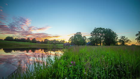 Das-Erwachen-Der-Morgensonne-Unter-Vorbeiziehenden-Wolken-Am-Grasbewachsenen-Flussufer