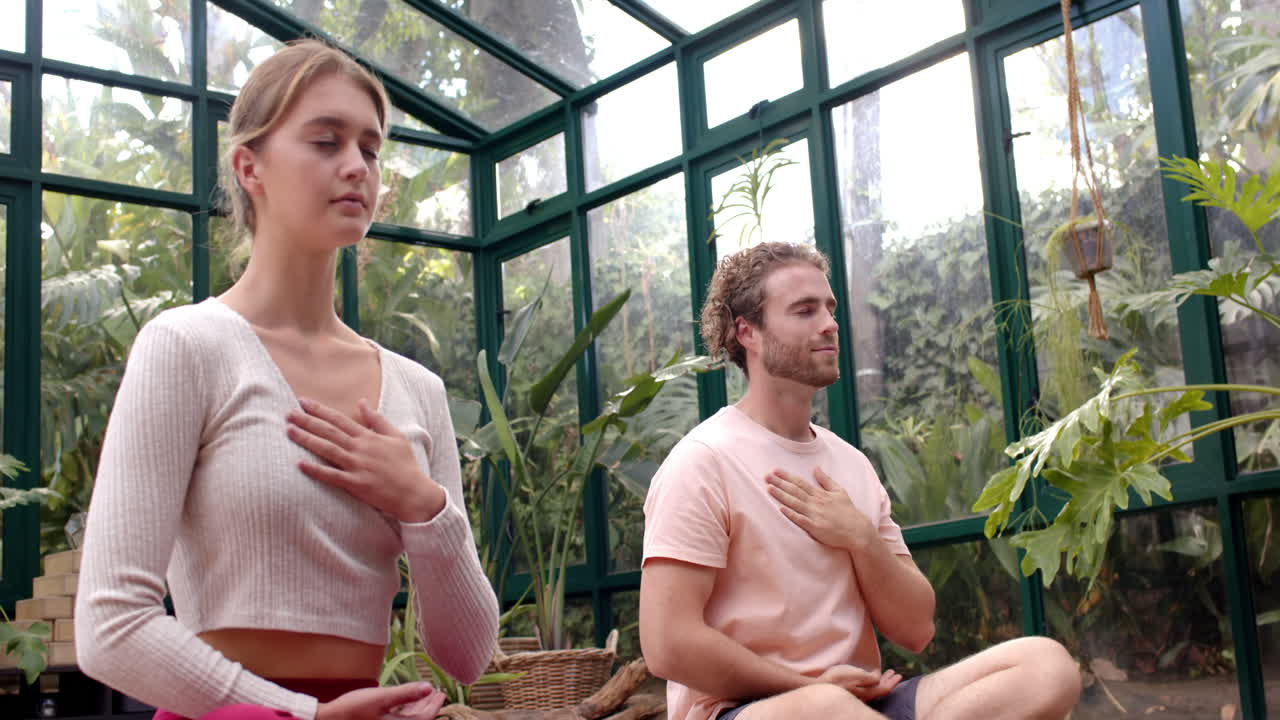 Practicing yoga, man and woman meditating with hands on chest in glass house