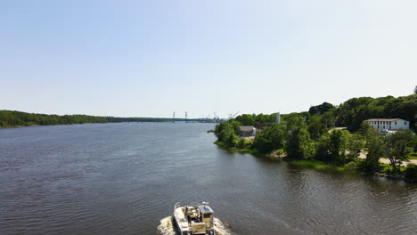 Drone-footage-flying-over-a-motorboat-on-the-Kennebec-River,-with-Bath-Water-Treatment-works,-with-Sagadahoc-Bridge-in-the-distance