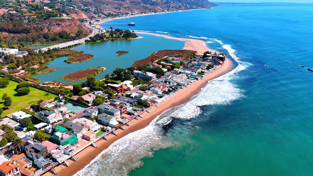 Beautiful foamy waves almost reach the line of the villas on the shore of the Pacific Ocean. Spectacular scenery of Malibu, Los Angeles County, California, USA on sunny day from drone