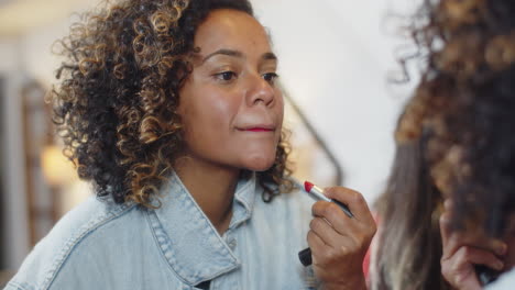 una mujer feliz de cabello rizado mirándose en el espejo y pintando los labios.