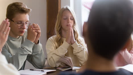 Group-of-students-and-teacher-praying-in-class