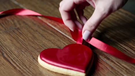 a hand tying a red ribbon around a heart-shaped cookie