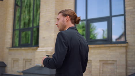 Side-view-man-using-tablet-while-going-to-work.-Businessman-waving-hand-outdoors